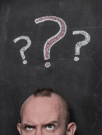 Closeup portrait of young man confused man isolated over black chalkboard with drawn question marks