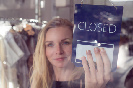 Pretty blond woman turning the open and closed sign in clothes shopの写真素材