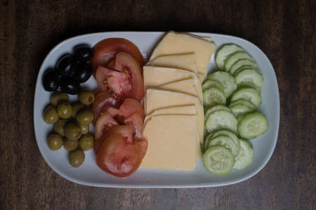 Closeup top view of plate with cheese and vegetables isolated on the wooden table backgroundの写真素材