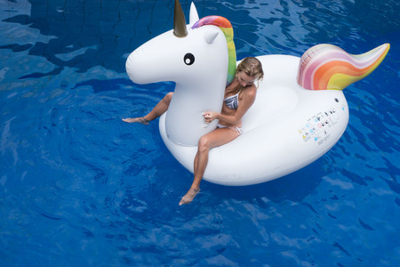 Top view of woman in bikini sitting on the big white inflatable unicorn in the poolの写真素材