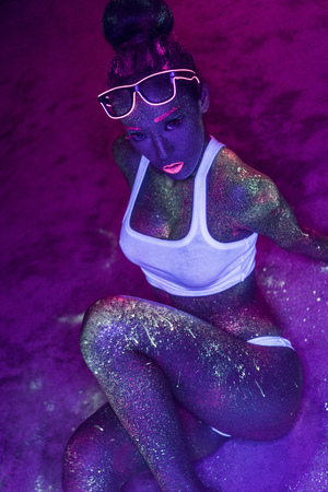 Sexy woman with fluorescent make up body and face posing on the concrete floor, creative makeup look great for nightclubs. Halloween party, shows and music concepの写真素材
