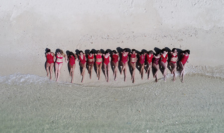 Aerial drone top view of happy women in red swimsuits sunbathing on the tropical sandy beachの写真素材