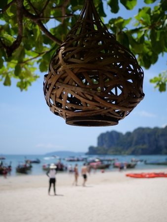 Wicker lantern at the tree over blurred silhouettes of people on the beach during sunny summer dayの写真素材
