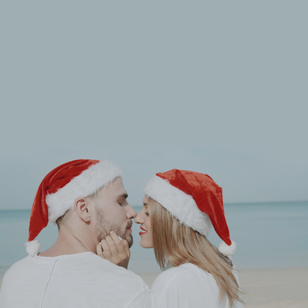 Christmas beautiful beach couple wearing Santa hat in summer sun in love on travel holidays on tropical travel destination during winter holidaysの写真素材