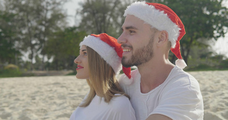 Christmas beautiful beach couple wearing Santa hat in summer sun in love on travel holidays on tropical travel destination during winter holidaysの写真素材