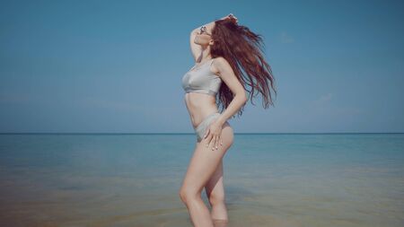 Beautiful girl in bikini and sunglasses relaxing on the tropical beach during summer holiday over sky backgroundの写真素材