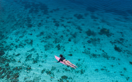 Aerial drone view of beautiful young woman in swimsuit and sunglasses with pink surfboard enjoying...