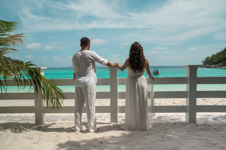 Attractive young couple on the tropical island. Beautiful woman and man wearing white clothes embracing each other and enjoying trpoical holidays vacation getawayの写真素材