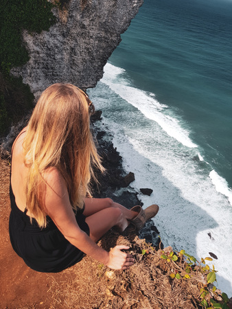 Top view of blonde woman tourist sitting on the cliff and admire beautiful ocean viewの写真素材