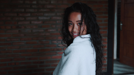 Beautiful lady after shower covered in white towel relaxing in her apartment. Portrait of fashion model girl indoorsの写真素材