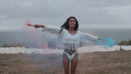 Beautiful happy girl with colored smoke playing at the mountain field over ocean and cloudy sky...