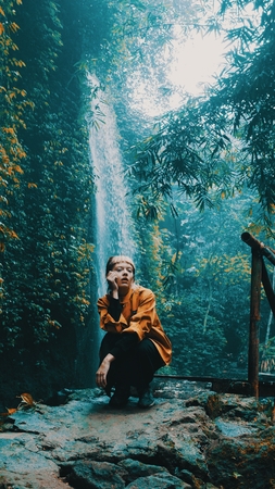 Beautiful fashion girl posing in tropical rain forest jungle near the waterfall. Portrait of stylish hipster female outdoor - vertical photo imageの写真素材