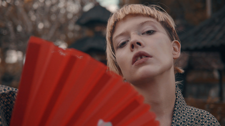 Portrait of beautiful fashion girl in kimono with red hand fan posing outdoor near traditional Balinese temple. Portrait of stylish hipster female outdoorの写真素材