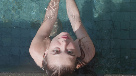 Top view of young pretty woman looking into the camera while relaxing in outdoor pool