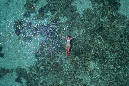 Aerial drone top view of woman floating in crystal clear sea water with coral reef