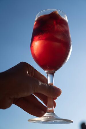 Hand serving Sangria with red wine in a glass isolated over blue summer skyの写真素材