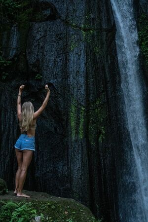 Aerial drone view back of woman looking at the beautiful waterfall in green tropical rain forest in...