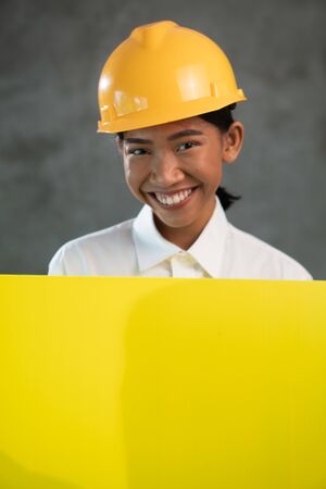 Portrait of smiling Asian woman engineer holding yellow board planover concrete wall backgroundの写真素材