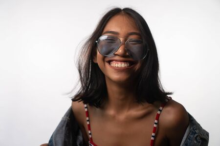 Portrait of smiling young Asian woman in sunglasses isolated over white wall backgroundの写真素材