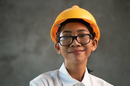 Portrait of smiling attractive Asian woman engineer over concrete wall background
