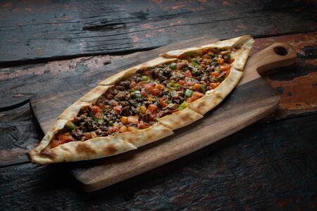 Turkish pide with beef and vegetables isolated on rustic wooden table