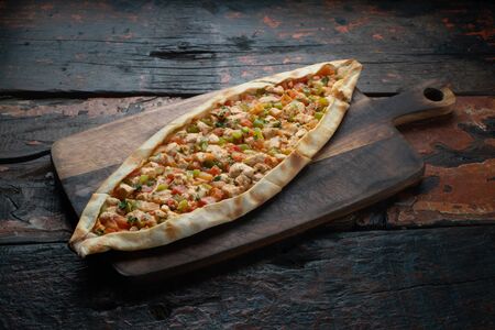 Turkish pide with chicken and vegetables isolated on rustic wooden tableの写真素材