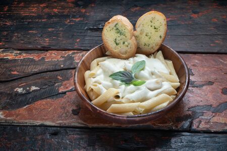 Four cheese pasta with garlic bread isolated on rustic wooden backgroundの写真素材