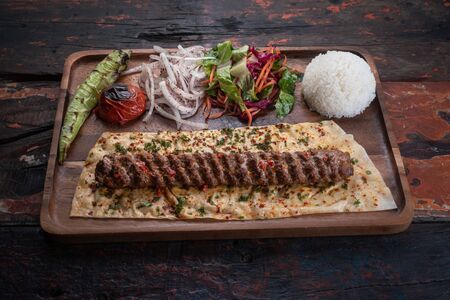Turkish lula lamb or beef kebab with rice and vegetables isolated on rustic wooden tableの写真素材