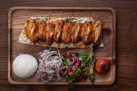 Turkish chicken wings kebab with rice and vegetables isolated on wooden table の写真素材