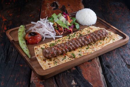 Turkish lula lamb or beef kebab with rice and vegetables isolated on rustic wooden table の写真素材