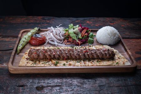 Turkish lula lamb or beef kebab with rice and vegetables isolated on rustic wooden tableの写真素材