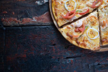 Closeup top view of fresh tasty pizza with seafood, tomato, paprika and mozzarella cheese isolated on rustic wooden backgroundの写真素材