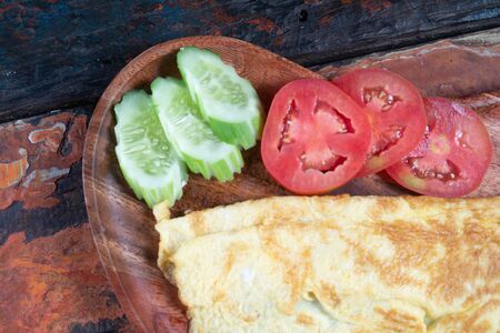 Closeup of plain egg omelette with tomato and cucumber isolated on rustic wooden backgroundの写真素材
