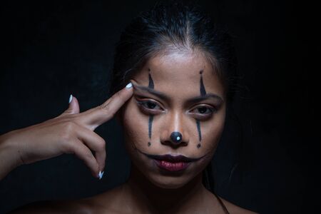 Halloween clown woman portrait committing suicide with finger gun gesture isolated over black walll backgroundの写真素材