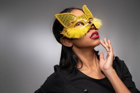 Portrait of attractive young Asian woman in gold cat carnival mask isolated over concrete wall backgroundの写真素材