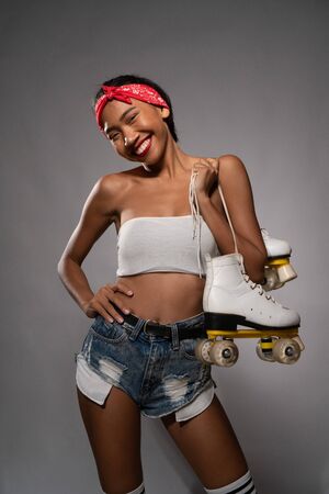 Young beautiful smiling Asian girl holding retro quads roller skates posing in studio over concrete wall backgroundの写真素材