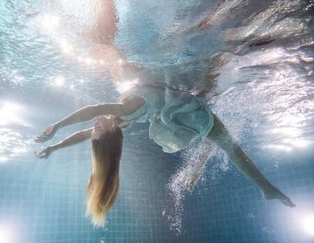 Beautiful woman with long red hair posing underwater in white dressの写真素材