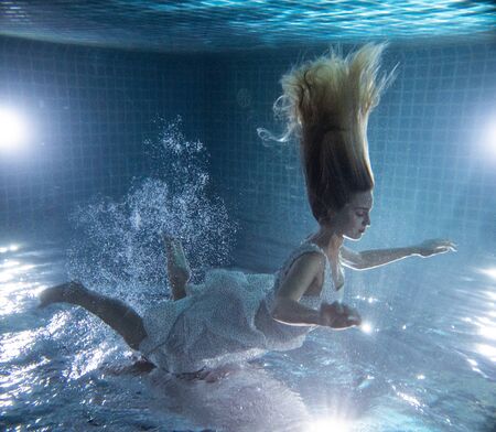 Beautiful woman with long red hair posing underwater in white dressの写真素材