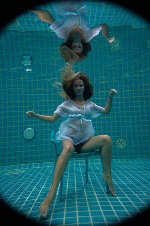 Beautiful woman with long red hair posing underwater on the chairの写真素材