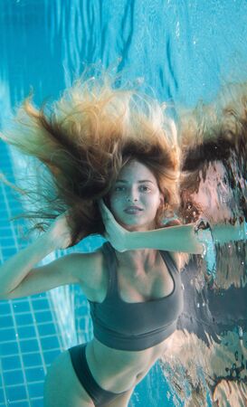 Beautiful woman with long red hair posing underwater in bikiniの写真素材