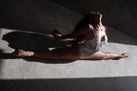 Beautiful acrobatic in white lace lingerie doing splits in the studio on concrete floorの写真素材