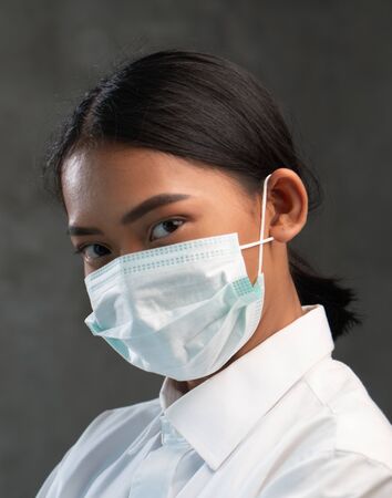 Young Asian woman wearing virus protection mask isolated over concrete wall background. Corona virus,covid-19 virus pandemic conceptの写真素材
