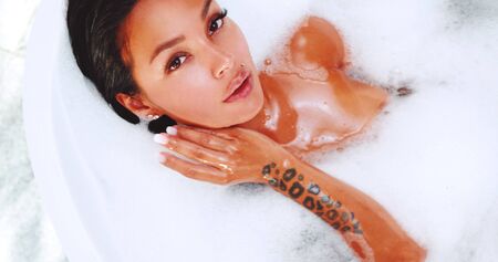 Top view portrait of beautiful and sensual brunette woman relaxing in bathtub with foamの写真素材