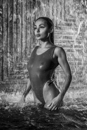 Beautiful brunette woman in swimsuit posing in outdoor pool over wall with waterfall background - black and white photographyの写真素材