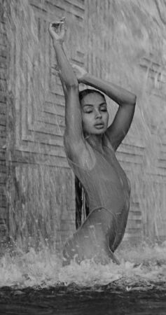 Beautiful brunette woman in red swimsuit posing in outdoor pool over wall with waterfall background - black and white photographyの写真素材
