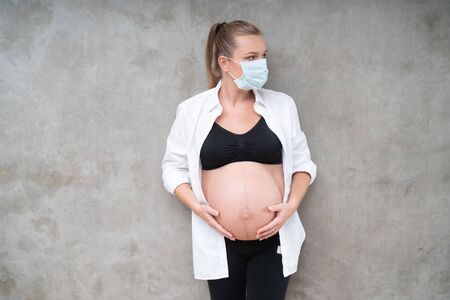 Pregnant woman in protective mask against flu and viruses on grey wall background. Healthcare conceptの写真素材