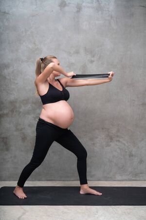 Portrait of pretty pregnant woman exercises with resistance band in the gym. Working out and fitness, pregnancy conceptの写真素材