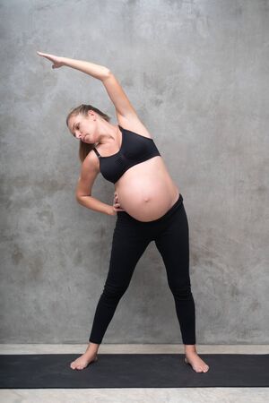 Portrait of pretty pregnant woman exercises on black mat in the gym. Working out and fitness, pregnancy conceptの写真素材