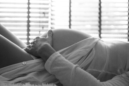 Closeup of pregnant woman lying in bed and touching her belly at home - black and white photographyの写真素材
