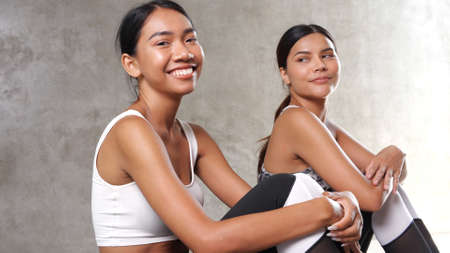 Two beautiful young Asian women taking break at the gym. Happy female friends spending their free time at the sport centreの写真素材